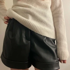 Svarta skinnshorts - Snygga svarta shorts i skinn med hög midja och breda uppvikta ben. Perfekta för en trendig look, dessa shorts har en stilren design med fickor och en elegant passform.