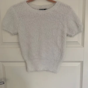 Vit stickad tröja från Zara - Säljer en söt vit stickad tröja från Zara. Den har korta ärmar och en rund halsringning. Perfekt för en stilren look. Tröjan är mjuk och bekväm, idealisk för både vardag och speciella tillfällen. Tröjan ser liten ut men är i ett strechigt material vilket gör att den passar för strl s. Använd få gånger.