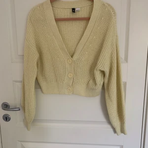 Gul stickad kofta från H&M Divided - Säljer en mysig och söt gul stickad kofta från H&M Divided. Koftan har en v-ringad design med knappar framtill och långa ärmar. Perfekt för att hålla sig varm och stilren under kyligare dagar.