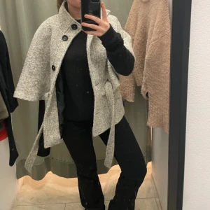 Grå kappa med knappar - Säljer nu min favorit jacka vid bra pris! Super snygg grå kappa med bälte och stora knappar. Den har en unik design med en cape-liknande stil och är perfekt för vår💘💘💘💘💘 Köpt i London!