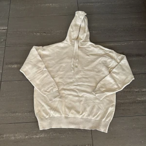 Beige stickad hoodie från Zara - Säljer en stilren beige hoodie från Zara. Den har en klassisk design med dragsko i huvan och ribbade muddar vid ärmslut och nederkant. Perfekt för en avslappnad look. Större storlek, passar främst L men även M