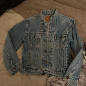 Blå jeansjacka från Levi's - Säljer en klassisk blå jeansjacka från Levi's med knappar framtill och två bröstfickor. Den är i fint skick. Vill bli av med snabbt så billigare vid snabb affär (kom med prisförslag)