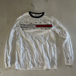 Vit långärmad tröja från Tommy Hilfiger - Säljer en vit långärmad tröja från Tommy Hilfiger med klassisk logga i svart och rött på bröstet. Tröjan har en rund halsringning med svart kant. Obs! Det står xl men den är barn xl, så mer mot xs-s. 