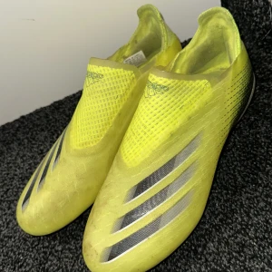 Gula fotbollsskor från Adidas - Snygga gula fotbollsskor från Adidas med svarta detaljer och en strömlinjeformad design. Skorna har en smidig passform utan snörning och är perfekta för snabba rörelser på planen.