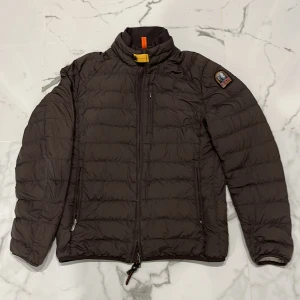Brun dunjacka från Parajumpers - Säljer en brun dunjacka från Parajumpers. Jackan har en dragkedja framtill och är långärmad med en quiltad design. Den är superlätt och har en snygg patch på ärmen. Perfekt för kyliga dagar! Jag har använt den ett par gånger och jag säljer denna för att den har blivit för liten 