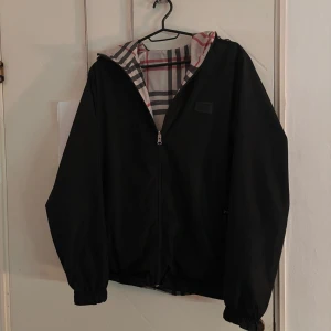 Svart vändbar burberry jacka  - Säljer en vändbar burberry jacka med svart utsida och rutig insida i beige, rött och svart. Jackan har dragkedja och långa ärmar, perfekt för höst och vår. Den rutiga sidan ger en klassisk look medan den svarta sidan är mer diskret. Det finns ett litet hål på framsidan av den svarta sidan men inget som syns jättemycket, pris kan diskuteras! Dragkedjan är sönder o saknas 