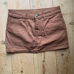Brun minikjol från H&M Divided - Snygg brun kortkjol från H&M Divided med klassisk jeansstil. Kjolen har fickor både fram och bak samt bälteshällor. Perfekt för en avslappnad look!