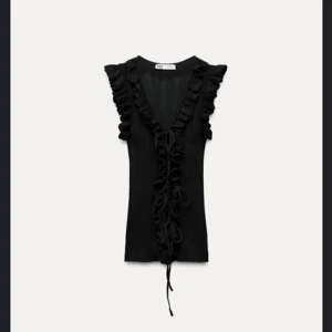 Svart ribbad topp med volangdetaljer - Snygg svart ribbad topp från Zara med volangdetaljer längs v-ringningen och ärmarna. Toppen har en knytning framtill som ger en extra touch!😊 Den är även helt ny, lappen är kvar och har endast provat den. Säljer eftersom att den var för stor. Ord pris 330kr