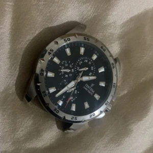 Svart klocka från Festina - Säljer en stilren klocka från Festina med svart urtavla och silverfärgade detaljer. Klockan har en robust design med tydliga markeringar och flera små urtavlor. Perfekt för den som gillar en sportig och elegant stil.