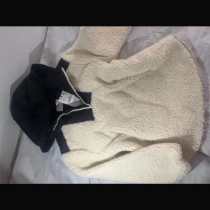 Vit teddyjacka med huva från Zara - Mysig beige teddyjacka från Zara med svart huva och dragkedja. Perfekt för kyliga dagar med sin mjuka och varma design. Jackan har en stilren look och är lätt att matcha med olika outfits.  I storlek 11-12 men funkar på storlek xxs-xs