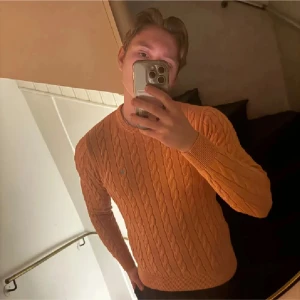 Orange stickad tröja med kabelmönster - Säljer en snygg orange stickad tröja med kabelmönster. Tröjan har långa ärmar och en rund halsringning. Perfekt för att hålla sig varm och stilren under kyligare dagar.