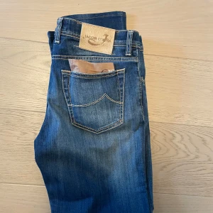 Jacob Cohen Jeans  - Säljer ett par snygga blå jeans från Jacob Cohen. De är handgjorda med exklusiva tyger och italienskt hantverk. Jeansen har en klassisk femficksdesign och en knappgylf. Perfekta för dig som vill ha stil och kvalitet i ett.