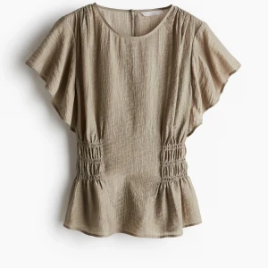 Beige blus med smockdetaljer - Säljer en stilren beige blus med korta ärmar och smockdetaljer i midjan. Blusen har en rund halsringning och ett lätt rynkat tyg som ger en fin struktur. Perfekt för en avslappnad men elegant look.