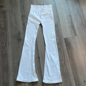 bootcut Vita ribbade tränings byxor  - Snygga vita ribbade träningsbyxor byxor från lager 157 med hög midja och utsvängda ben. Byxorna är tillverkade i ett stretchigt material som ger en bekväm passform. aldrig använda. storleken är mindre än ärr, längden är ungefär som M. jag säljer dom för att dom är alldeles för långa för mig.