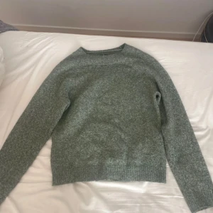 Grön stickad tröja från Vero Moda - Säljer en mysig grön stickad tröja från Vero Moda i storlek XS. Tröjan har en klassisk design med långa ärmar och ribbstickade muddar vid ärmslut och nederkant. Perfekt för kyliga dagar!