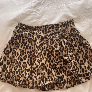 Leopardmönstrad kortkjol Gina Tricot - Snygg kortkjol från Gina Tricot med trendigt leopardmönster i bruna och svarta toner. Kjolen har bred resår i midjan för skön passform och är lätt utställd för en cool look. Perfekt att matcha med en enkel topp eller hoodie.