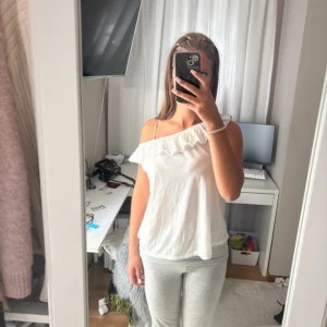 Vit offshoulder topp med volang - Supersöt vit offshoulder topp från H&M med volang längs halsringningen. Toppen är ärmlös och har en luftig passform, perfekt för varma dagar. Tillverkad i mjuk bomull som känns skön mot huden. Enkel att styla 