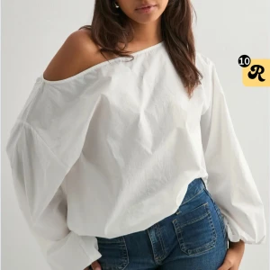 Vit offshoulder blus  - Snygg vit blus med offshoulder-design och vida, långa ärmar. Toppen har en lös passform och är tillverkad i ett lätt bomullstyg som ger en fräsch och luftig känsla. Perfekt för dig som gillar en stilren och trendig look. Aldrig använd