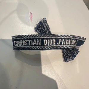 Christian Dior J'Adior armband blå - Snyggt armband från Christian Dior med texten 'J'Adior' broderad i vitt på blå bakgrund. Inga fel på detta armband plus att den är super fin.