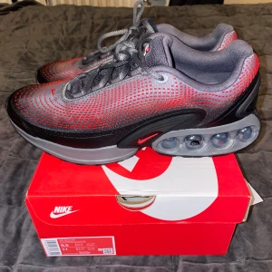 Nike Air Max DN Svart/Röd Sneakers - Nike Air Max DN sneakers i svart och rött med grå detaljer. Ovandel i mesh med coolt prickigt mönster och synlig Air Max-dämpning i sulan. Skickas med shoeboxen.