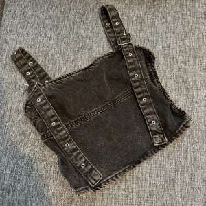 Svart jeanskorsett från Zara - Cool svart korsettopp från Zara i jeansmaterial med justerbara axelband med spännen och snygg dragkedja bak. Smockade sidor för extra passform och edgy look. Perfekt att styla med höga jeans eller kjol för en trendig vibe.