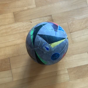 Euro 2024 fotboll - Bilderna visar en fotboll från Adidas med färgglada mönster och tydliga tecken på användning. Den är perfekt för dig som gillar att spela fotboll med vänner på fritiden och vill ha en boll med cool design. Passar både till spontana matcher och träning.