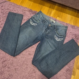 Vintage jeans med broderi och pärlor - Snygga blå jeans från Rogin med unika broderade detaljer och pärlor på fickorna. Jeansen har raka ben, normal passform och coola nitar längs fickorna. Perfekta för dig som vill sticka ut med lite extra detaljer i din outfit. Tror att dem är low waist. Dem är vintage eftersom dem är 19 år gamla!!! Från min mamma