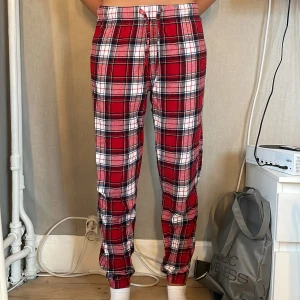 Rödrutiga mjukisbyxor XS med snörning - Supermysiga rödrutiga mjukisbyxor i bomull med snörning i midjan och muddar vid bensluten. Perfekta för chill hemma eller sleepovers. Klassisk rutig design i rött, vitt och svart. Sitter skönt och har relaxed fit.