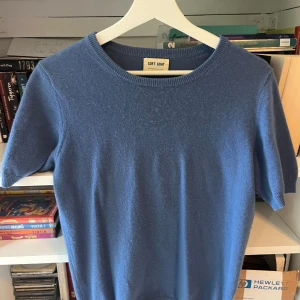 Blå kashmirtröja från Soft Goat - Superskön blå tröja från Soft Goat i 100% kashmir. Modellen har korta ärmar, rund halsringning och ribbade muddar. Perfekt för dig som vill ha en mjuk och stilren tröja med lyxig känsla. Passar lika bra till jeans som till kjol.