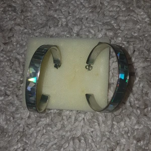 Stora silvriga örhängen med glittrig yta - Säljer ett par stora silvriga hoops med glittrig yta som reflekterar ljuset snyggt. Örhängena har en bred design och stängs med klassisk plopp. Perfekta för dig som vill sticka ut lite extra. PRIS KAN DISKUTERAS!