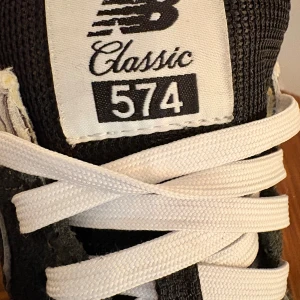 New Balance 574 Classic sneakers grå - Snygga New Balance 574 Classic sneakers i grå mocka och mesh med vita detaljer och snörning. Ikonisk N-logga på sidan och vit hälkappa med svart New Balance-tryck. Perfekta för en sportig och stilren look.