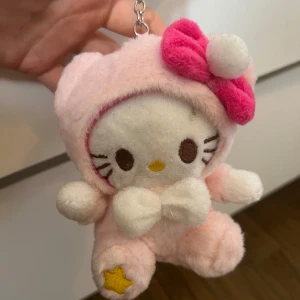 Hello Kitty rosa plysch plånbok - Supersöt Hello Kitty nyckelring i mjuk plysch med ljusrosa färg och en stor rosa rosett. Perfekt att hänga på väskan.