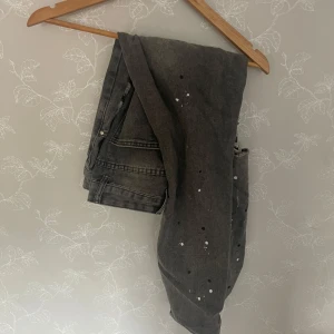 Grå slitna jeans med färgstänk - Säljer ett par grå jeans med coola slitningar och vita färgstänk. Byxorna har klassisk femficksmodell, raka ben och normal passform. Perfekta för dig som gillar en edgy streetstil. Materialet är jeans i bomull.