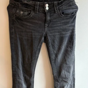 Svarta jeans från Gina Tricot, stl 158 - Gråa jeans från Gina Tricot i klassisk femficksmodell. Jeansen är lowaist och bootcut , dubbla knappar i midjan och snygga slitningar för en cool look. Tillverkade i mjukt bomullsmaterial med stretch för extra komfort.