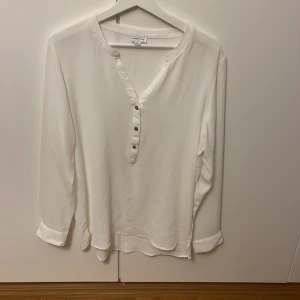 Vit henley från Jacqueline de Yong - Säljer en stilren vit henley-skjorta från Jacqueline de Yong i storlek 40. Skjortan har lång ärm, v-ringning och tre knappar framtill. Materialet känns lätt och flowy, perfekt för en clean och enkel look.