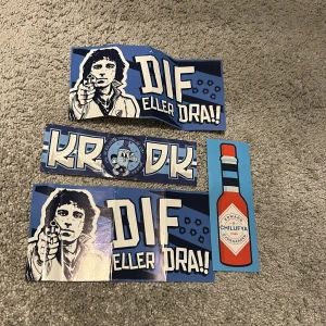 DIF eller dra! / KRODK / Edward Chilufya - Samling med klistermärken i blått och vitt med motiv och texter kopplade till Djurgårdens IF. Perfekt för unga supportrar som vill visa sitt stöd för laget på ett kreativt sätt.