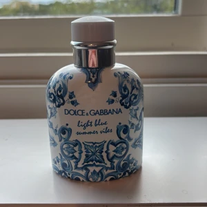 Dolce & Gabbana Light Blue Summer Vibes - Snygg parfymflaska på 125 ml från Dolce & Gabbana, Light Blue Summer Vibes. Flaskan är vit med blått, detaljerat mönster och har en rundad form med silverfärgad spray och vit kork. Eau de toilette för honom, tillverkad i Italien, mer än halva kvar.