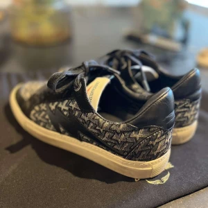 Zadig & Voltaire  sneakers  - Snygga svarta sneakers från Zadig & Voltaire med unikt grått mönster och svarta skinn- och textildetaljer. Skorna har rund tå, platt sula och svarta snören. Perfekta för dig som vill sticka ut med en cool och modern stil.