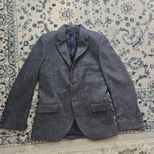 Mörkgrå kavaj från Hackett London - Snygg mörkgrå kavaj från Hackett London med klassisk passform. Kavajen har tre fickor framtill, knappar vid ärmslut och är helfodrad med ett stilrent innerfoder. Perfekt för dig som vill ha en stilren och tidlös look.