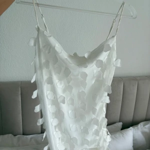 Vit långklänning med 3D-detaljer - Superfin vit långklänning med tunna axelband och unika 3D-bladliknande detaljer över hela klänningen. Sval och flowy känsla. Materialet känns lätt och elegant, och modellen är figurnära men ändå avslappnad, detta är en mermaid modell så klänningen lägger sig jätte fint. Aldrig använd - enbart legat nerpackad, den är köpt från Gina Tricots säsong 2024 och var då slutsåld överallt. Nypris 699:- ❤️