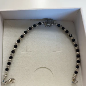 Armband med elefant och pärlor - Snyggt armband med små svarta och silvriga pärlor samt en detalj i form av en silverfärgad elefant i mitten. Perfekt accessoar för att ge din outfit lite extra personlighet.