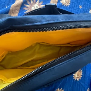 Blå axelväska från We Power - Säljer en blå axelväska från We Power med flera dragkedjefack och justerbar rem. Insidan är fodrad i gult och väskan har coola detaljer som patch och svarta dragkedjor med gula inslag. Perfekt för att bära dina grejer på ett smidigt sätt.