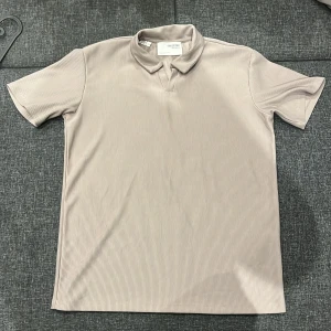 Beige ribbad t-shirt Selected Homme - Snygg beige t-shirt från Selected Homme med ribbad struktur och klassisk krage. T-shirten har korta ärmar och en stilren, diskret look som passar perfekt till jeans eller chinos. Materialet känns mjukt och följsamt mot huden.