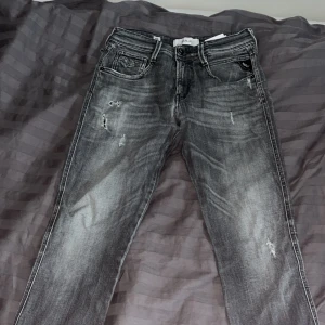 Replay grå slitna jeans - Säljer ett par grå jeans från Replay med snyggt slitna detaljer och tvättad look. Jeansen har klassisk femficksdesign, dragkedjegylf och raka ben. Replay Anbass, slim fit.