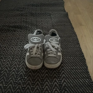 Grå Adidas Campus sneakers - Grå Adidas Campus sneakers. Fina men hål i ovansidan vid hälen. Men det är inget som syns på utsidan. Har satt dit en svart tyg bit för att täcka hålet och de funka bra. 