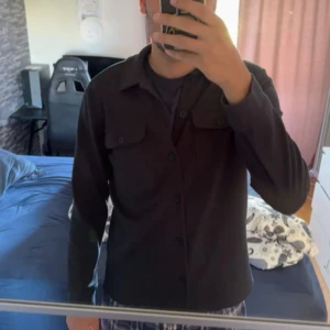 Svart overshirt från Only & Sons M - Säljer en svart overshirt från Only & Sons i storlek M. Skjortan har klassisk krage, knäppning framtill och två bröstfickor med lock. Perfekt att slänga över en t-shirt för en clean look. Materialet känns mjukt och följsamt.