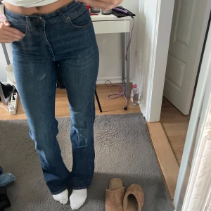 Mörkblå bootcut midwaist jeans från Wrangler - Snygga mörkblå jeans från Wranglee med bootcut passform och hög midja. Klassisk femficksmodell med Wrangler-logga på bakfickan. Jeansen är i ett stretchigt denimtyg som sitter bekvämt och ger en schysst siluett.