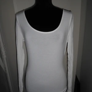 Vit långärmad topp med u-ringning - En basic vit långärmad topp med rundad halsringning både fram och bak. Tunn och mjuk, perfekt att styla med jeans eller kjol. Sitter tight mot kroppen och är enkel att matcha med allt. Aldrig använd.