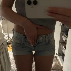 Ljusblå jeansshorts från Pepe Jeans - Säljer ett par ljusblå jeansshorts från Pepe Jeans med låg midja. Klassisk femficksmodell, råa kanter nertill och snygga detaljer med logga på bakfickan. Perfekta till sommaren och lätta att matcha med allt.