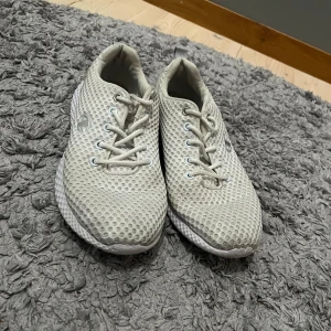 Vita träningsskor från Champion - Snygga vita sneakers från Champion med luftig mesh-ovandel och klassisk snörning. Skorna har en chunky, strukturerad sula och diskret logga på sidan. Perfekta för dig som gillar sportig och clean stil.